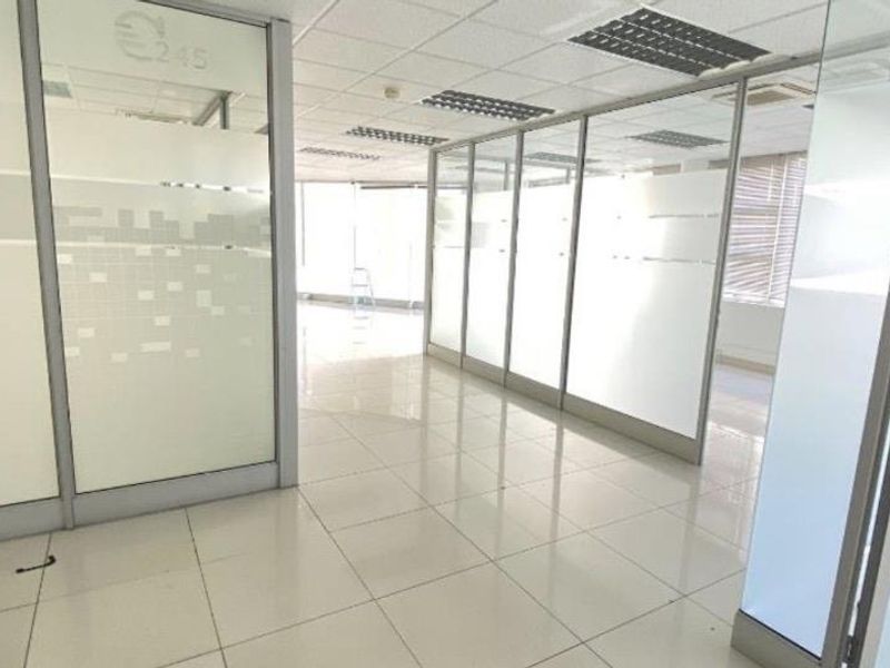 Modern office space featuring glass partition walls, suspended ceilings with recessed lighting, and clean tiled flooring, offering a bright and professional work environment.