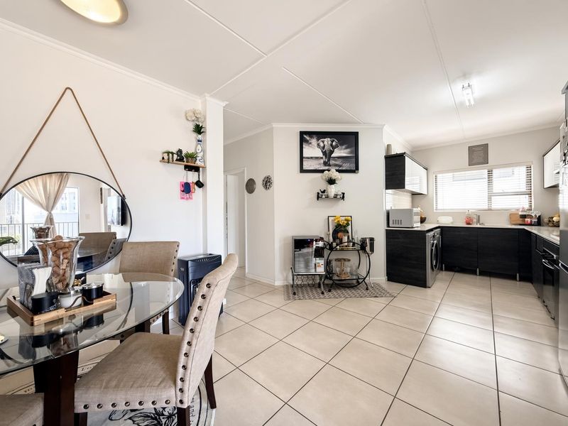 An open-plan living and kitchen area featuring tiled flooring, modern dark cabinetry, and a functional layout with integrated laundry appliances.