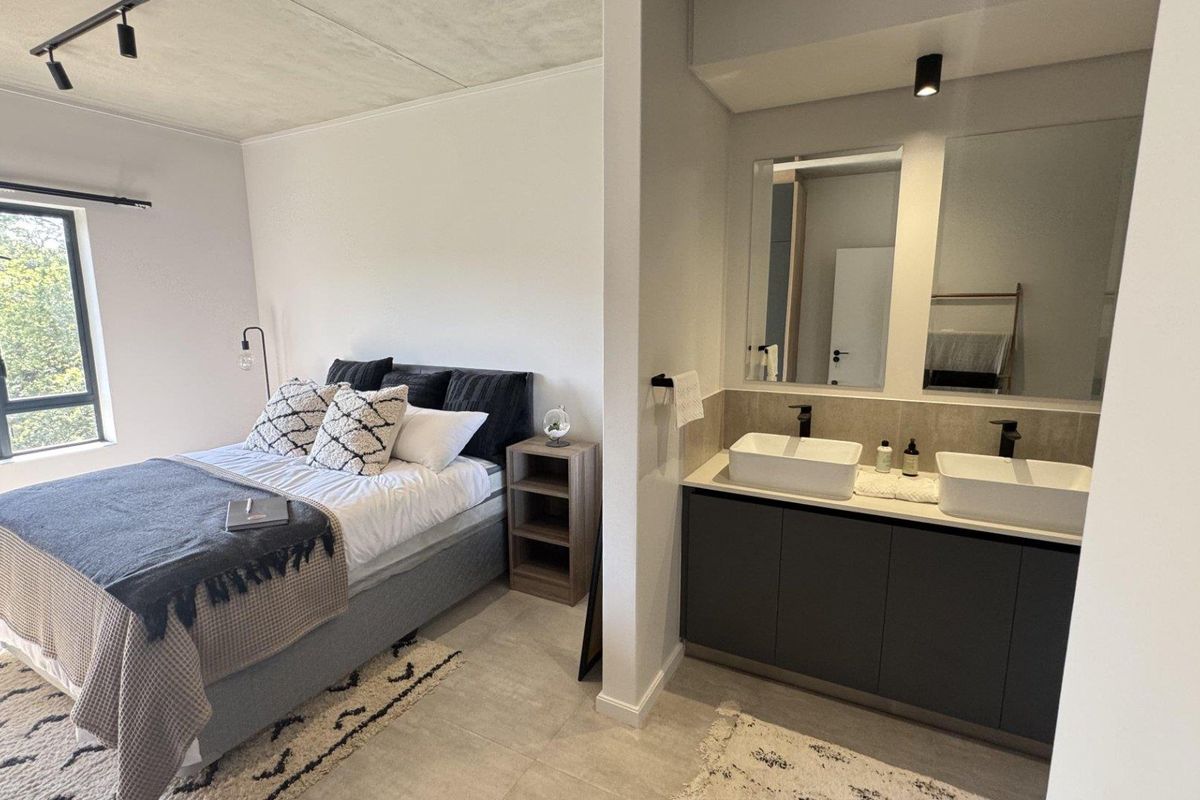 Modern open-plan bedroom featuring a contemporary en-suite bathroom with dual vessel sinks, dark cabinetry, and large mirrors.