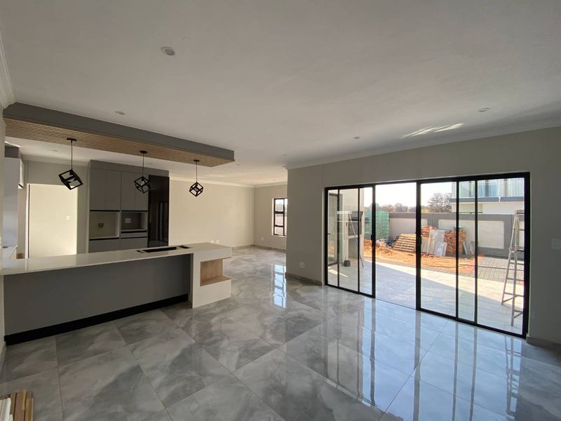 Modern open-plan living area featuring a sleek kitchen island, high-gloss cabinetry, and large sliding glass doors opening to an outdoor patio space.