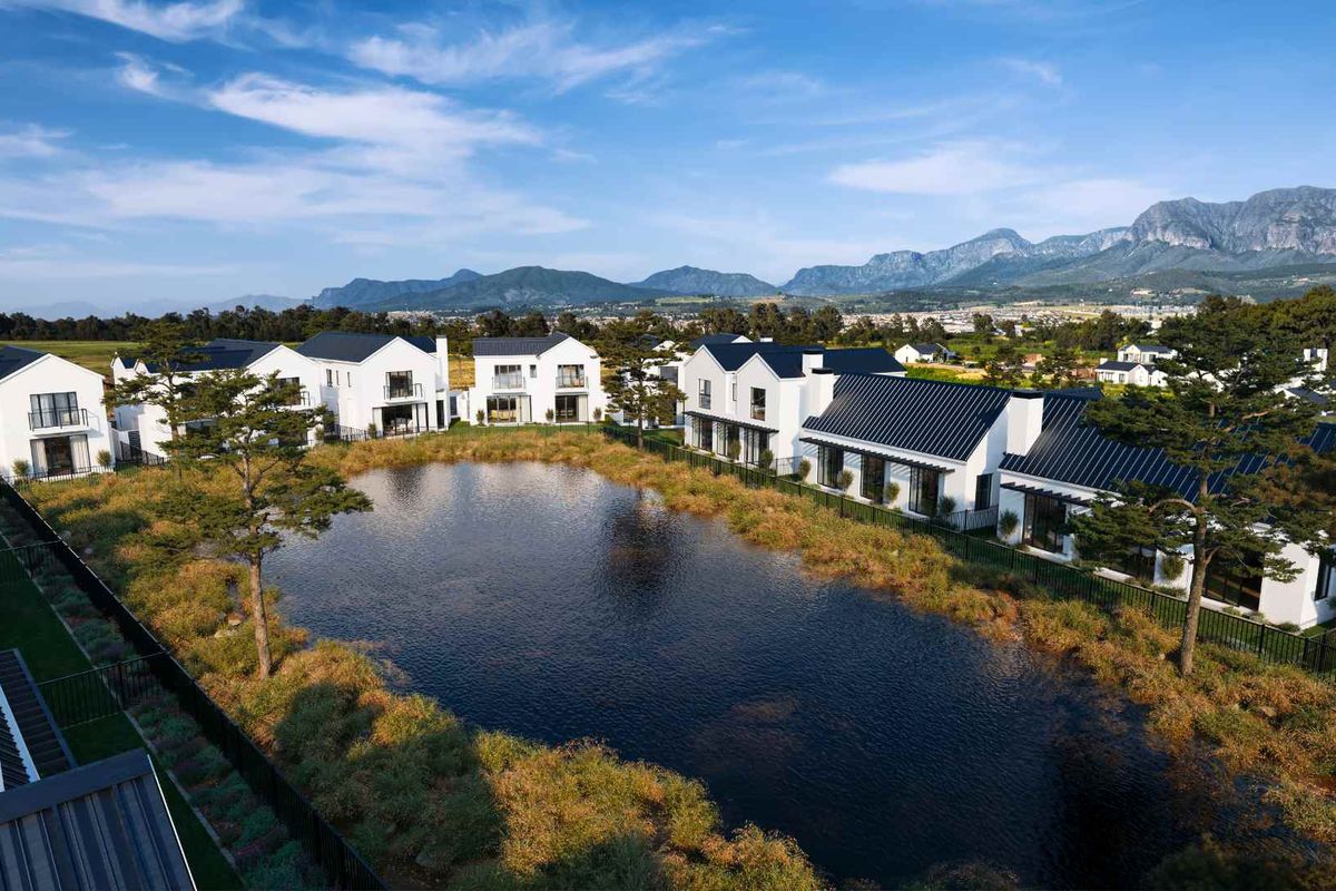 Aerial view of a modern residential estate featuring white homes with dark metal roofs surrounding a central pond and landscaped grounds.