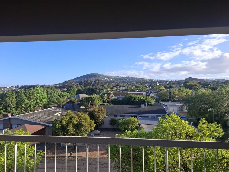 Elevated view overlooking a suburban neighborhood with lush greenery and a prominent mountain in the background, framed by a balcony railing.