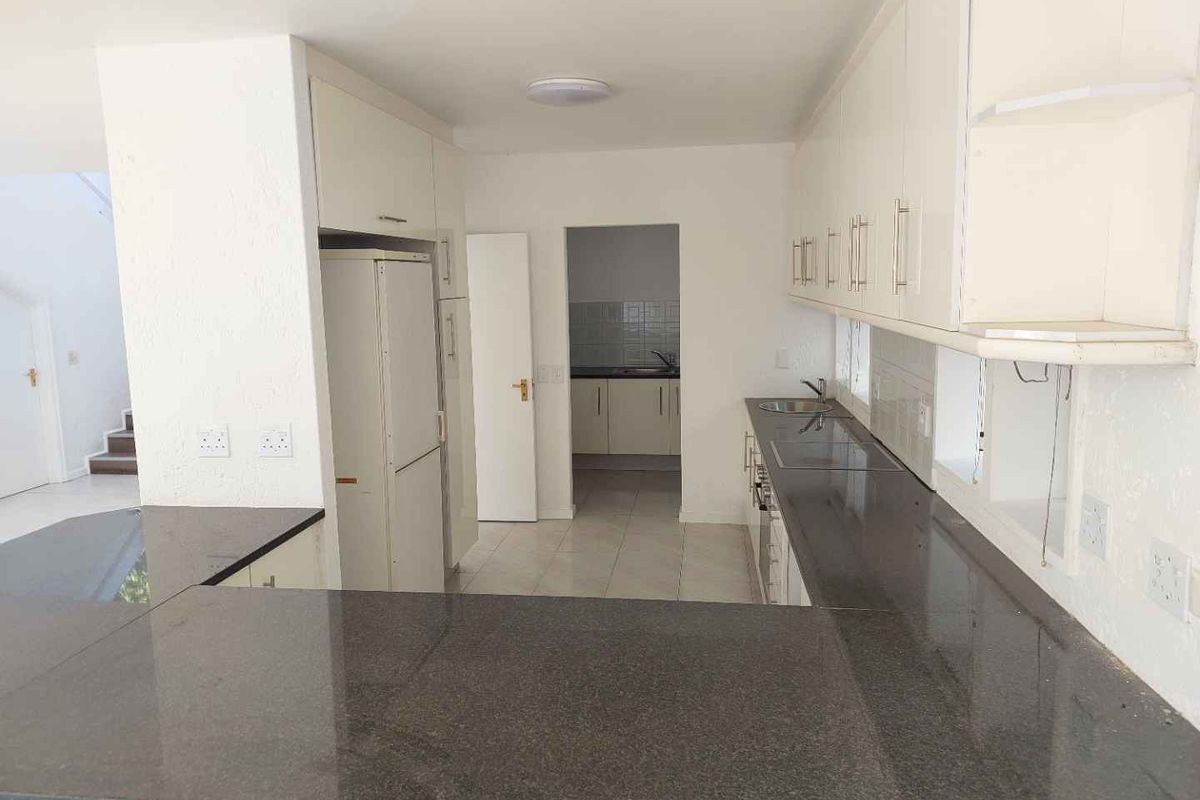 A functional kitchen featuring granite countertops, ample built-in cabinetry, and an adjoining scullery area, offering a clean and practical layout for daily use.