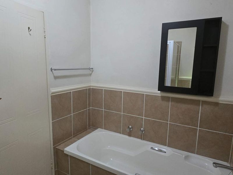 A functional bathroom featuring a built-in bathtub with tiled splashback, a wall-mounted mirror cabinet, and a towel rail.