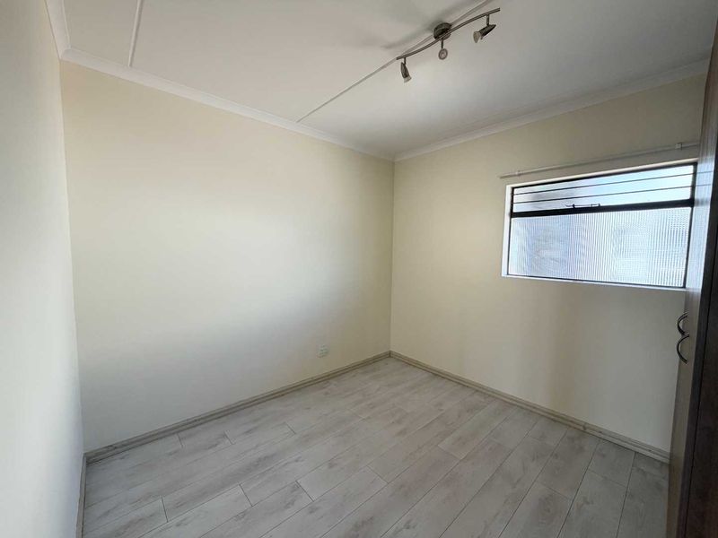 A clean, empty bedroom featuring light-toned laminate flooring, a built-in cupboard, and a window with obscured glass for privacy.