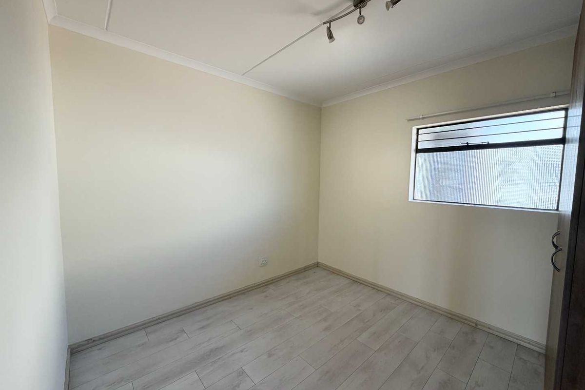 A clean, empty bedroom featuring light-toned laminate flooring, a built-in cupboard, and a window with obscured glass for privacy.