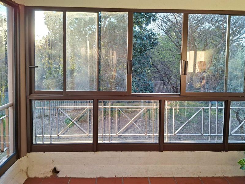 Enclosed balcony area featuring terracotta flooring, sliding glass doors with integrated security bars, and views of the surrounding garden.