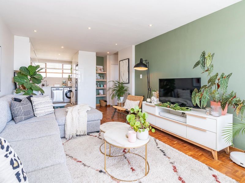Bright open-plan living area featuring parquet flooring, a green accent wall, and an integrated kitchen space with modern finishes.