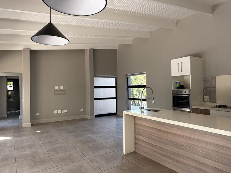 Spacious open-plan living and kitchen area featuring modern cabinetry, a central island, tiled floors, and high exposed beam ceilings with abundant natural light.