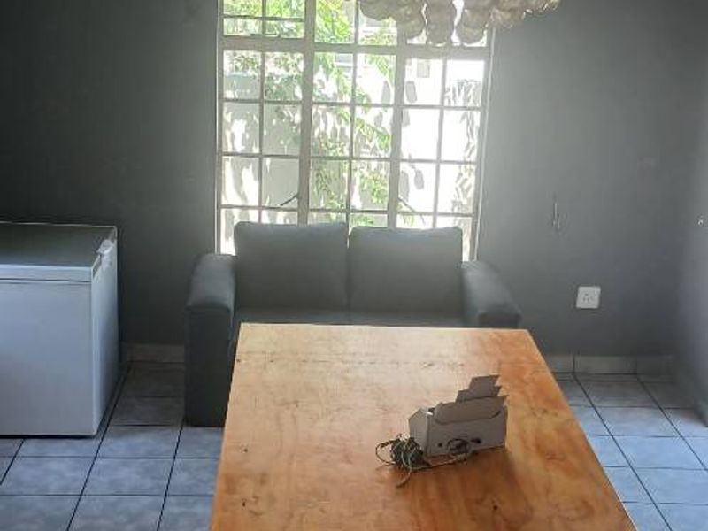 A living area featuring grey walls, tiled flooring, and a prominent crystal chandelier, offering a blank canvas for potential interior updates.