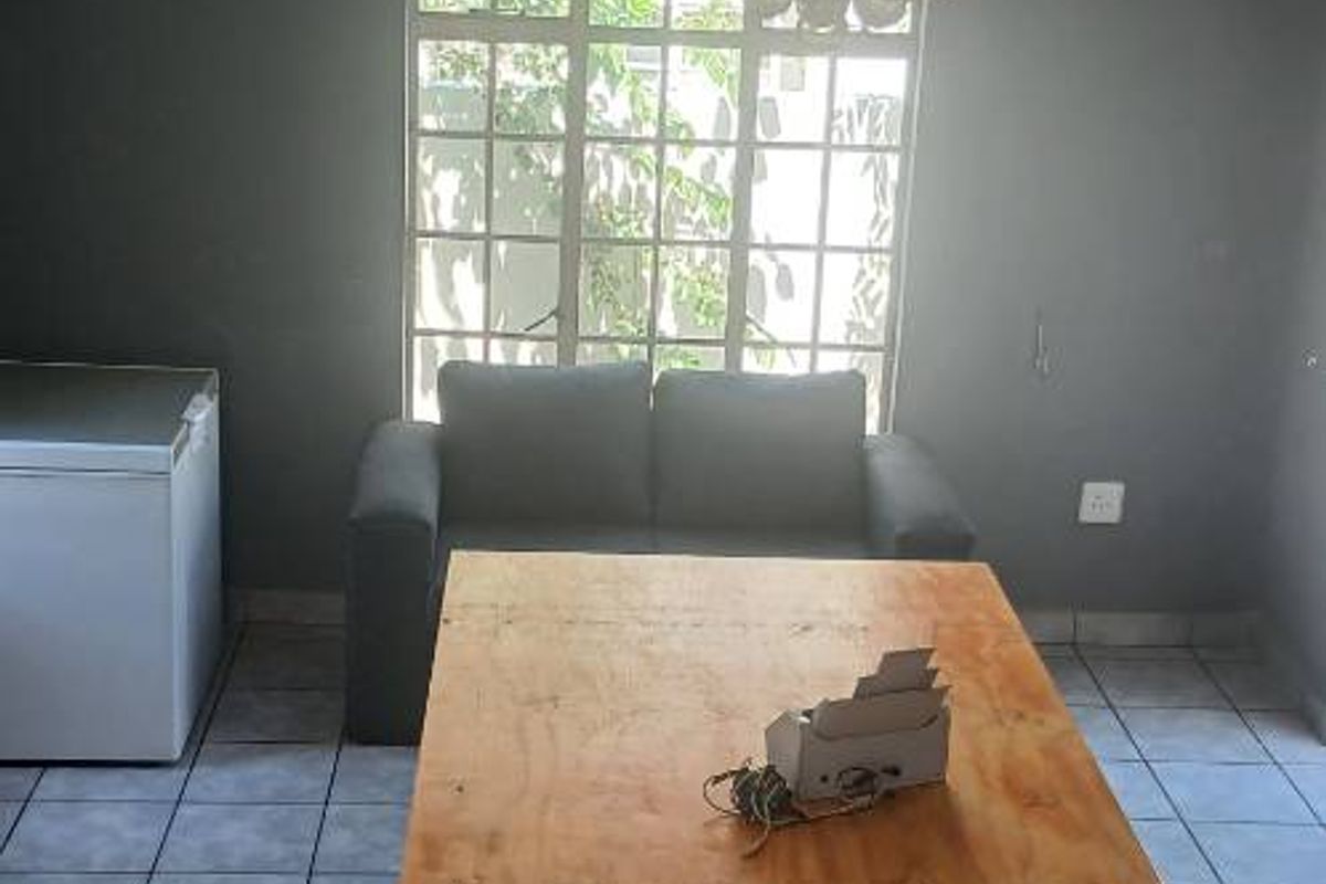 A living area featuring grey walls, tiled flooring, and a prominent crystal chandelier, offering a blank canvas for potential interior updates.