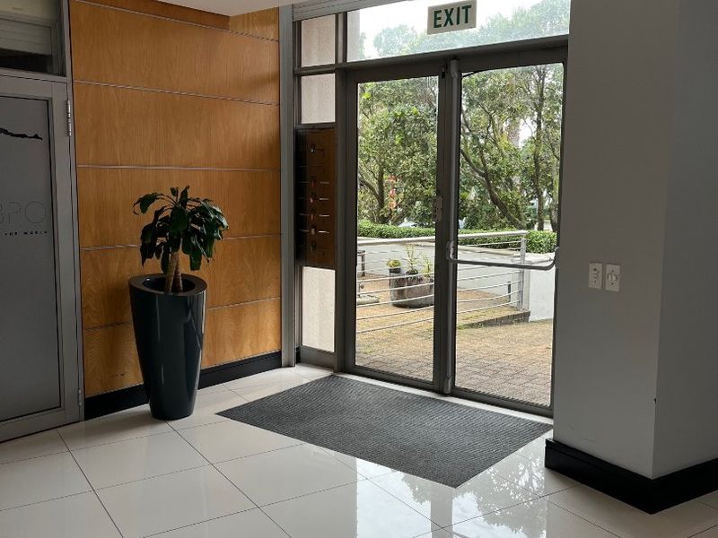 A bright and modern office building entrance featuring polished tiled floors, wood paneling, and glass double doors leading to an outdoor area.