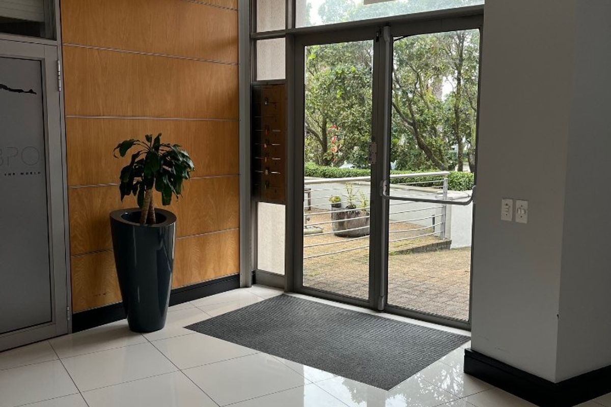 A bright and modern office building entrance featuring polished tiled floors, wood paneling, and glass double doors leading to an outdoor area.