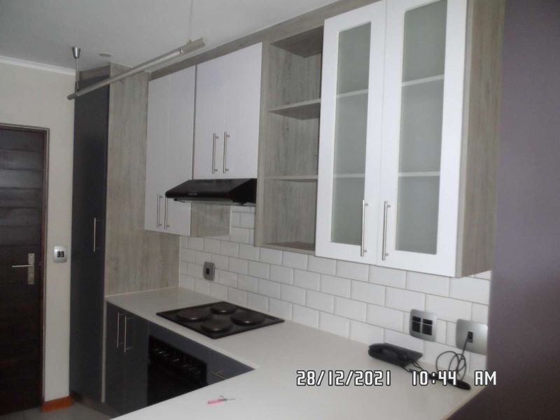 Modern kitchen featuring white and wood-tone cabinetry, subway tile backsplash, integrated electric hob, oven, and extractor fan.
