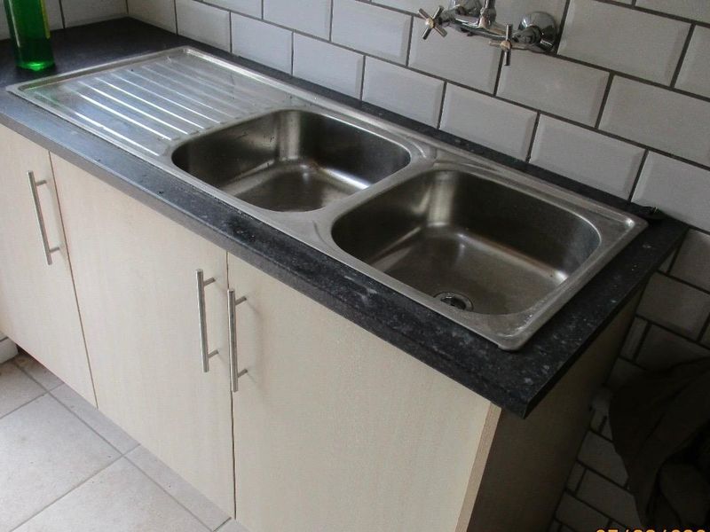 A functional kitchen sink area featuring a double bowl stainless steel sink, laminate countertop, and white subway tile backsplash.
