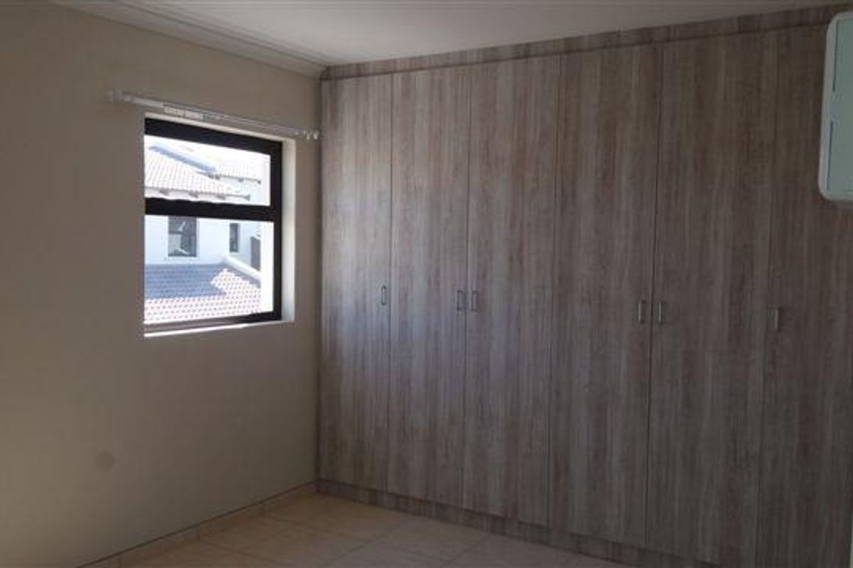 A bedroom featuring built-in wooden cabinetry and tiled flooring, offering functional storage space and natural light.