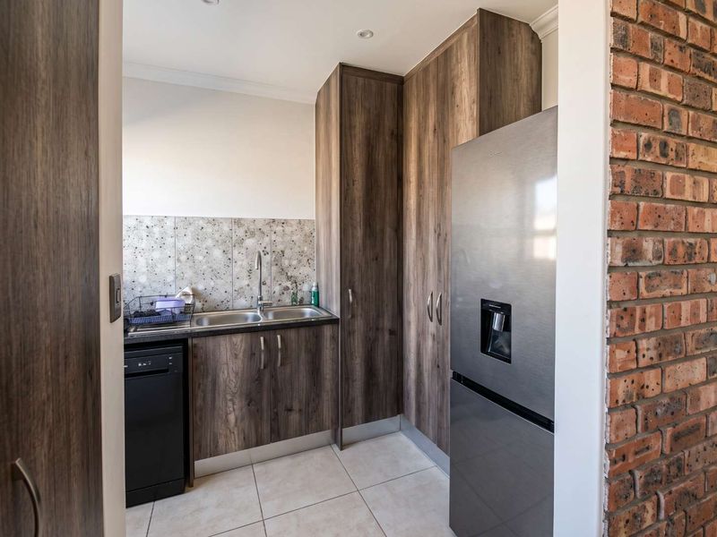 A functional scullery featuring modern wood-look cabinetry, a double sink, tiled splashback, and an exposed brick feature wall.