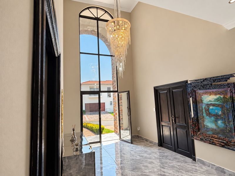 Grand double-volume entrance hall featuring high ceilings, a large arched window, elegant tiled flooring, and sophisticated dark wood door frames.
