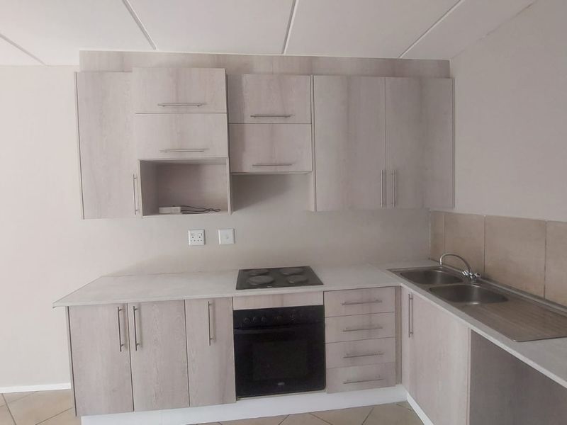 A clean, functional kitchen featuring light wood-finish cabinetry, integrated electric hob and oven, and a double stainless steel sink with tiled splashback.