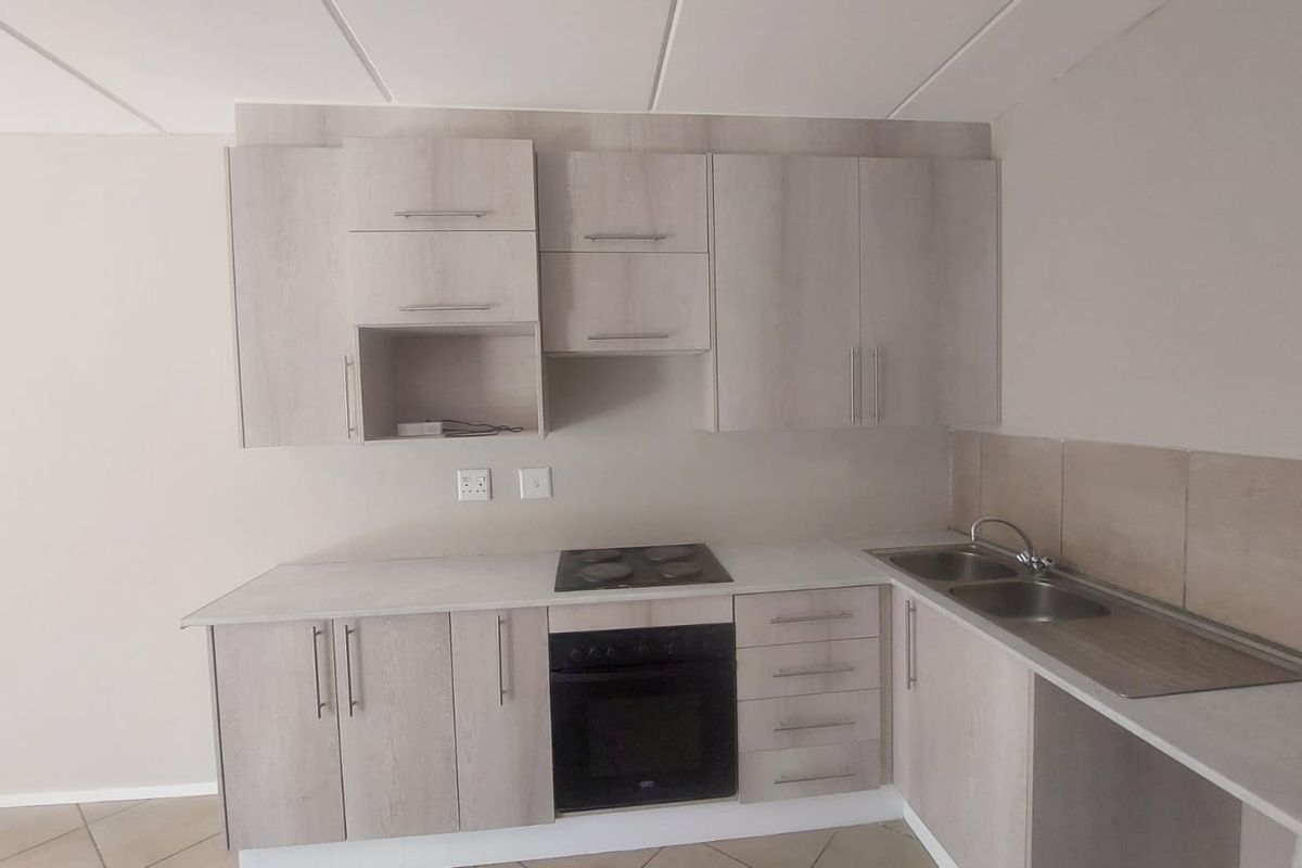 A clean, functional kitchen featuring light wood-finish cabinetry, integrated electric hob and oven, and a double stainless steel sink with tiled splashback.