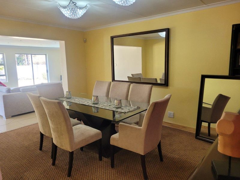 A dining room featuring a crystal chandelier, cove cornicing, and tiled flooring, with an open-plan layout connecting to the adjacent living area.