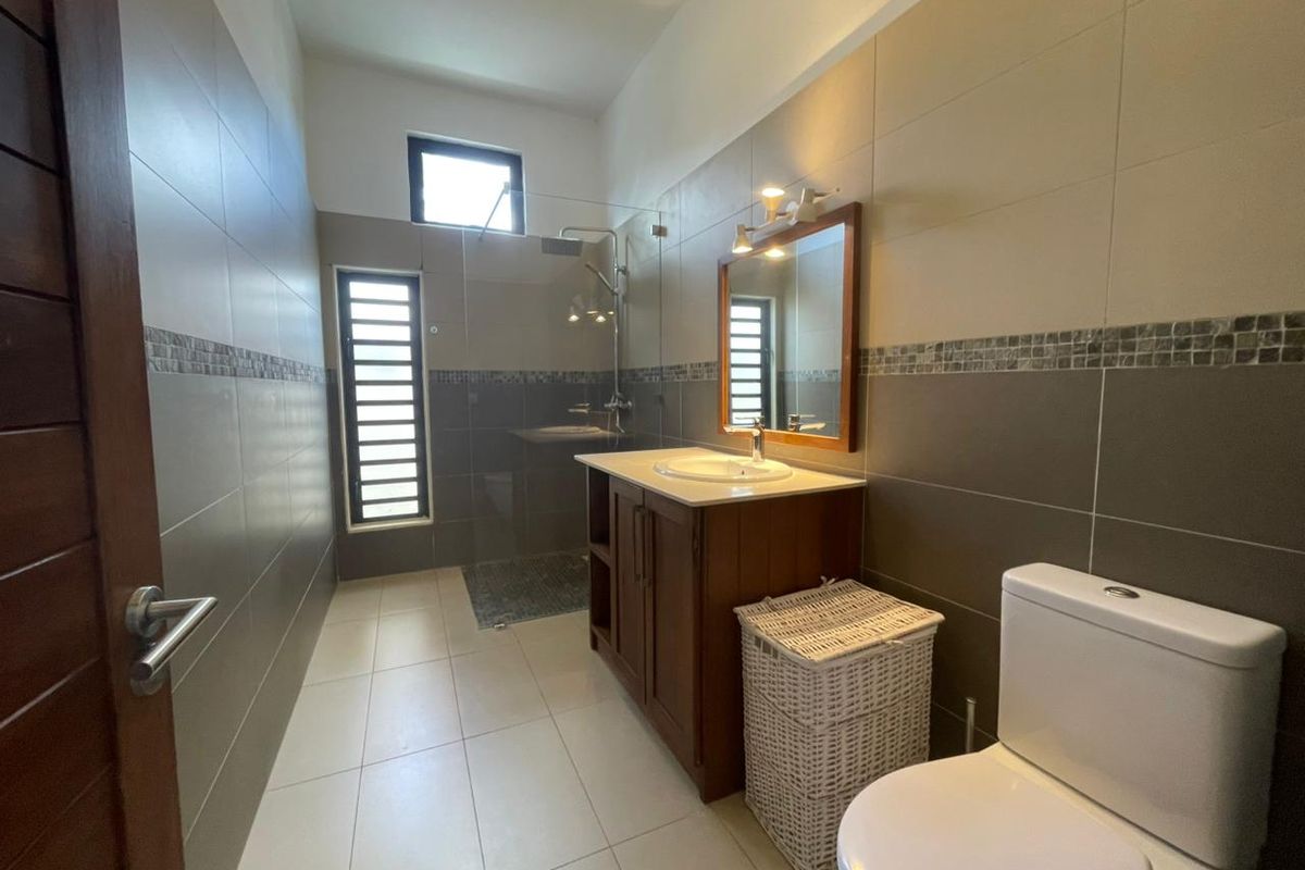 A modern bathroom featuring a glass-enclosed walk-in shower, a wooden vanity with a basin, and neutral wall tiling.