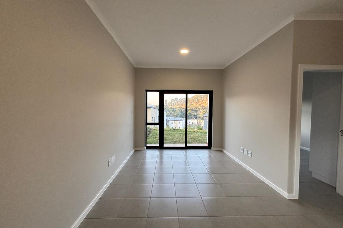 A bright, empty living area featuring neutral tiled flooring, recessed lighting, and a sliding glass door providing access to the outdoor space.