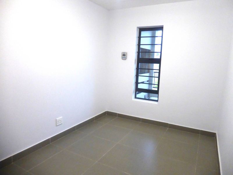A clean, empty bedroom featuring neutral tiled flooring, a window with security bars, and a wall-mounted thermostat.