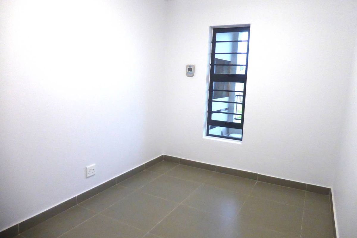 A clean, empty bedroom featuring neutral tiled flooring, a window with security bars, and a wall-mounted thermostat.