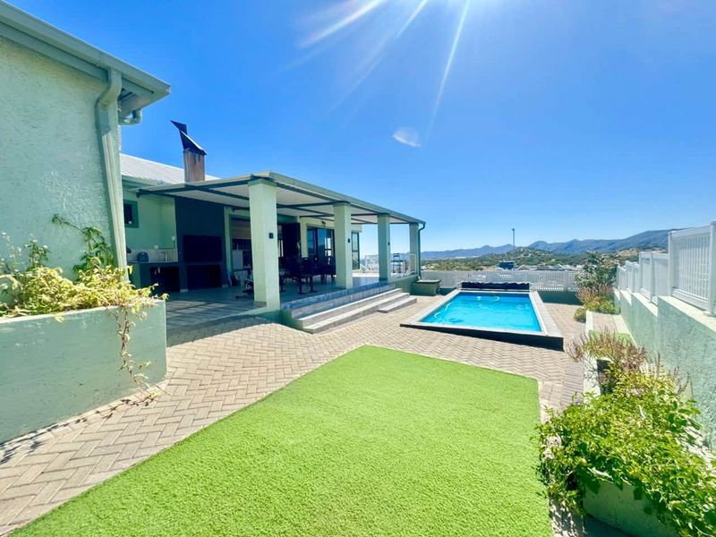Outdoor entertainment area featuring a swimming pool, covered patio with built-in braai, and paved courtyard with mountain views.
