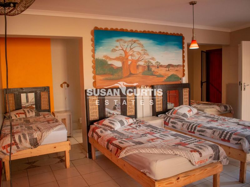 A spacious bedroom featuring tiled flooring, neutral wall finishes, and multiple bed placements, suitable for guest house accommodation.