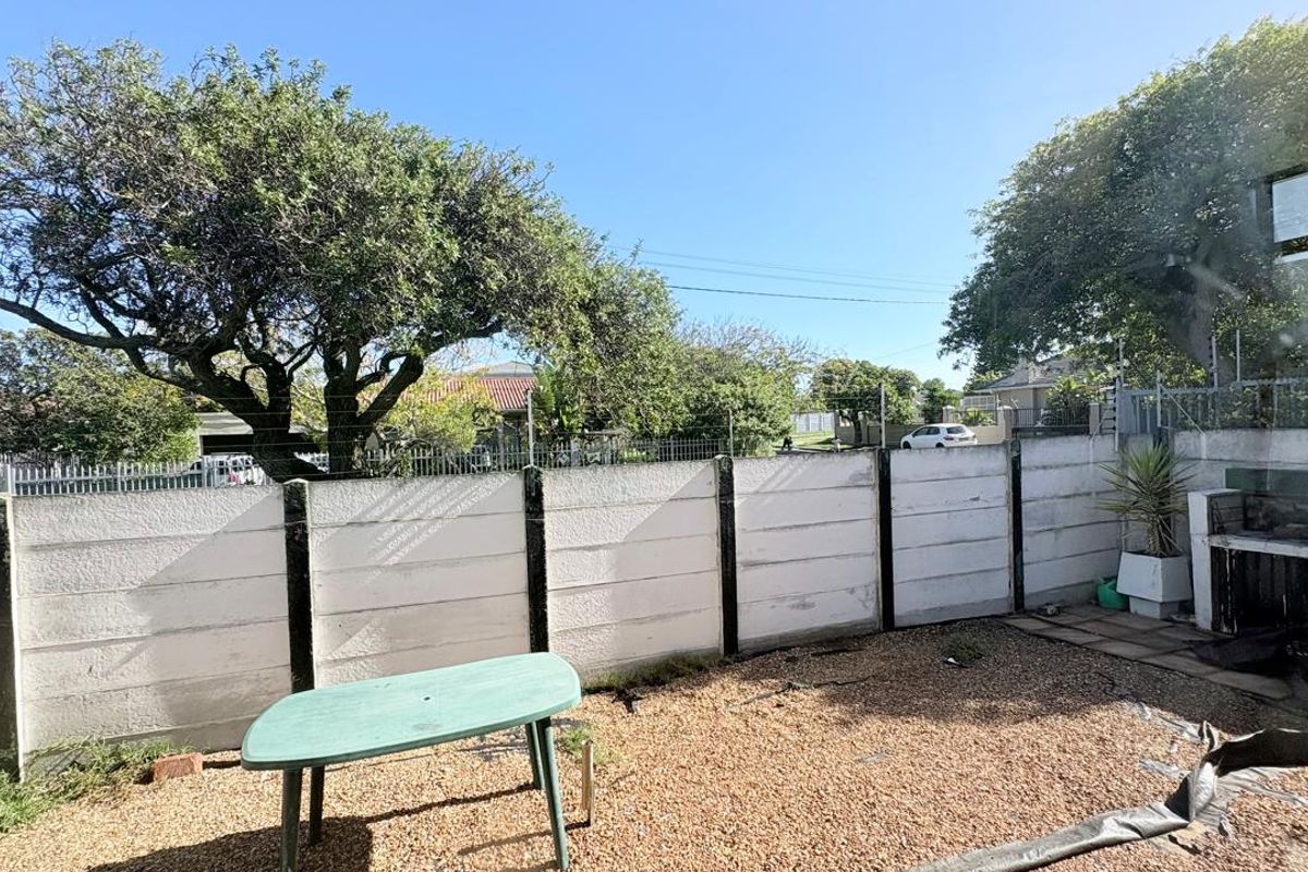 A private rear courtyard featuring a precast concrete boundary wall, gravel ground cover, and a built-in masonry braai area.