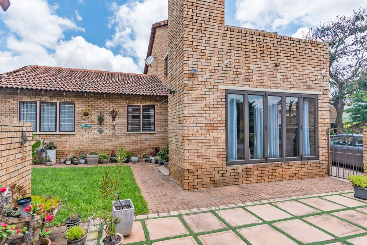 Rear view of a face brick townhouse featuring a paved patio area, well-maintained lawn, and aluminium framed windows with security bars.