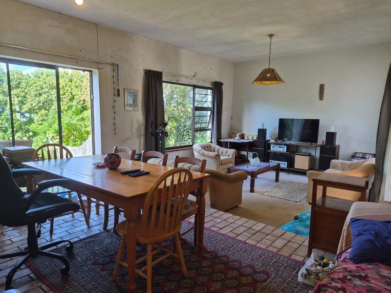 Spacious open-plan living and dining area featuring brick flooring, large windows, and sliding door access to the outdoors, requiring cosmetic updates.