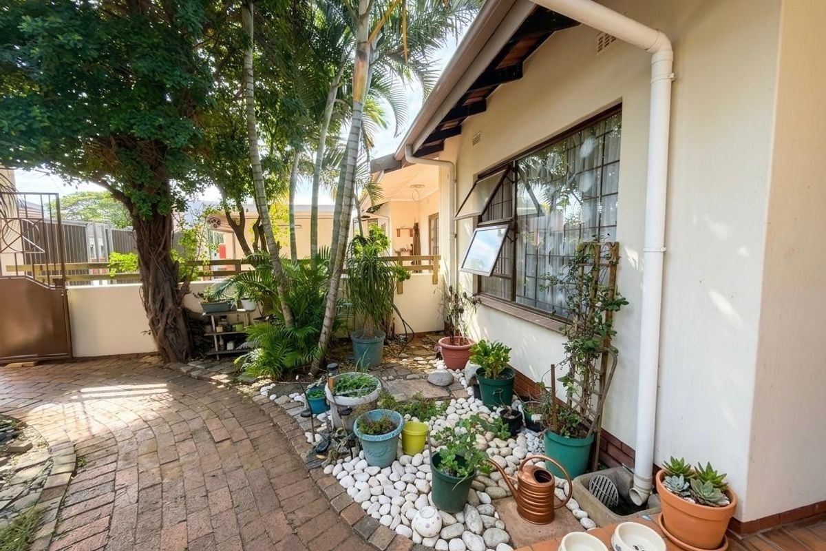 A private rear courtyard area featuring brick paving, established trees, and a side elevation of the townhouse with a casement window.