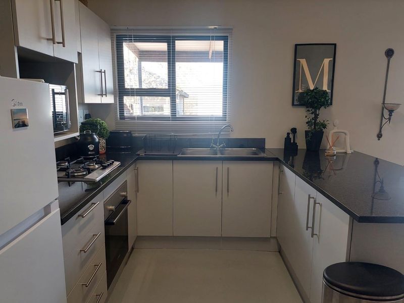 A functional kitchen featuring modern white cabinetry, dark granite countertops, a gas hob, and a built-in oven, complemented by a window for natural light.