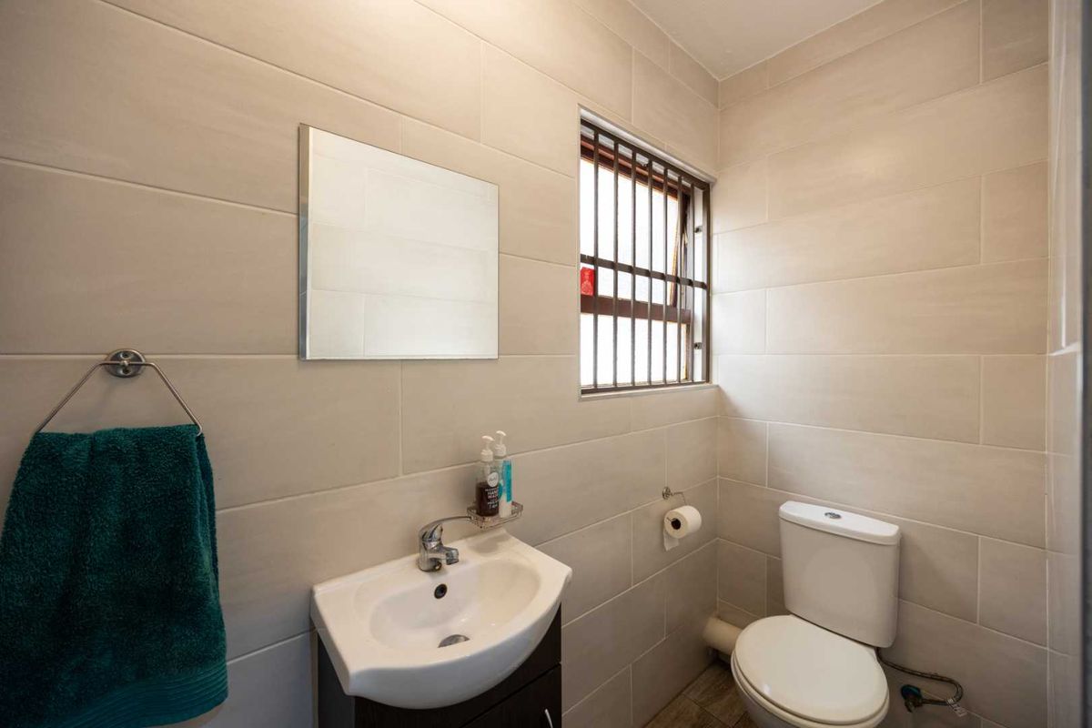 A compact, modern bathroom featuring neutral wall tiles, a vanity basin, and a toilet, with security bars installed on the window.