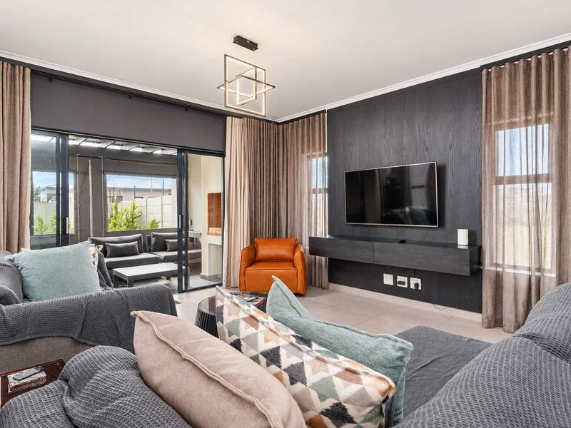 A modern, well-appointed living room featuring a sleek built-in media console, contemporary lighting, and large sliding doors that open to an outdoor patio area.