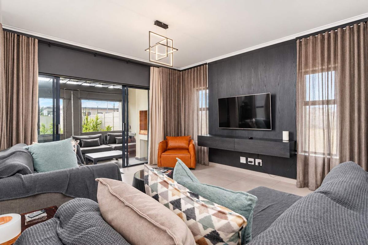 A modern, well-appointed living room featuring a sleek built-in media console, contemporary lighting, and large sliding doors that open to an outdoor patio area.