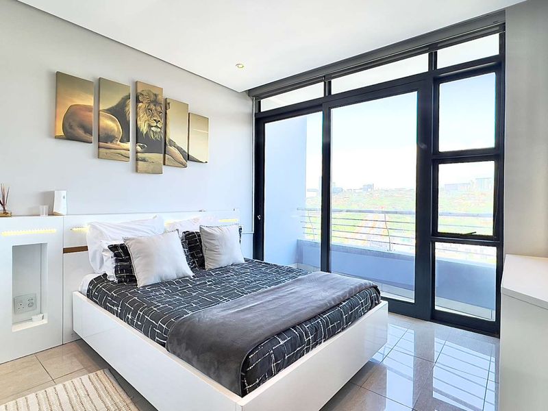Modern bedroom featuring tiled floors, a built-in headboard with integrated lighting, and large sliding glass doors opening to a private balcony with city views.