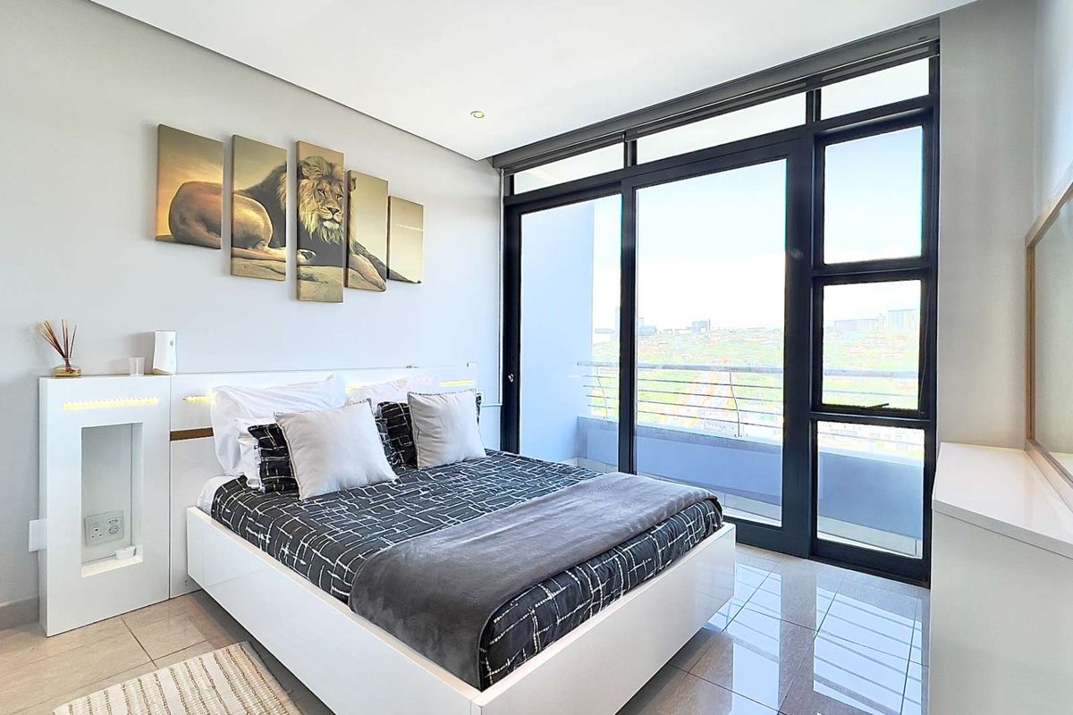 Modern bedroom featuring tiled floors, a built-in headboard with integrated lighting, and large sliding glass doors opening to a private balcony with city views.
