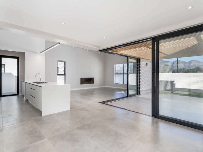 Modern open-plan living area featuring a sleek kitchen island, fireplace, and seamless indoor-outdoor flow through large sliding glass doors to a covered patio.