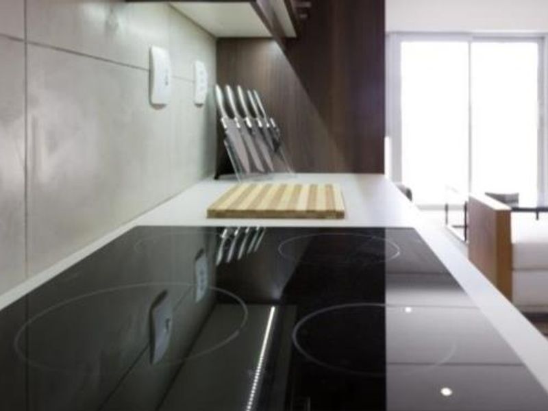 Modern kitchen area featuring a sleek electric hob, tiled backsplash, and integrated under-cabinet lighting, overlooking an open-plan living space.