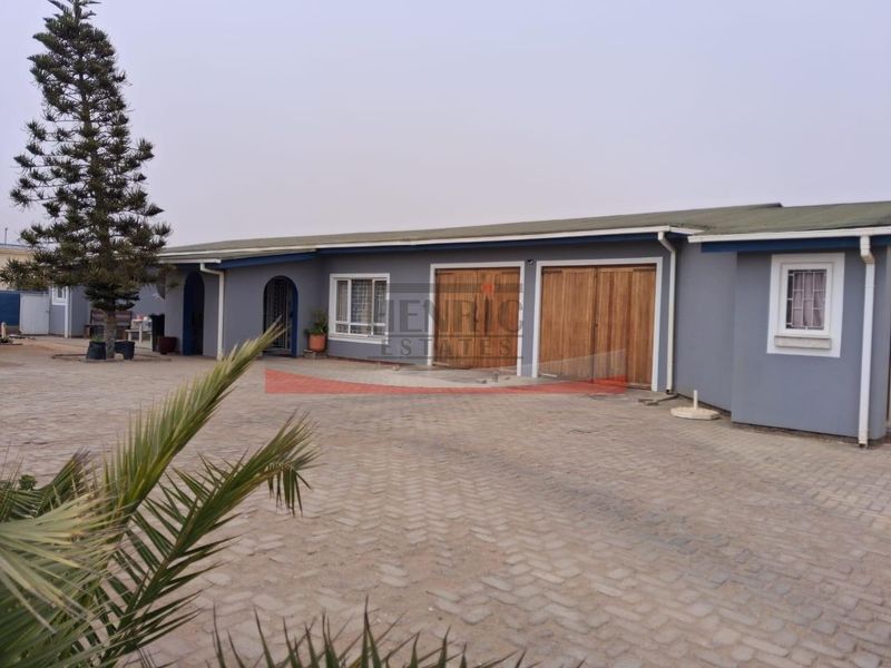 Front exterior view of the property featuring a spacious paved driveway and a double garage with timber doors.