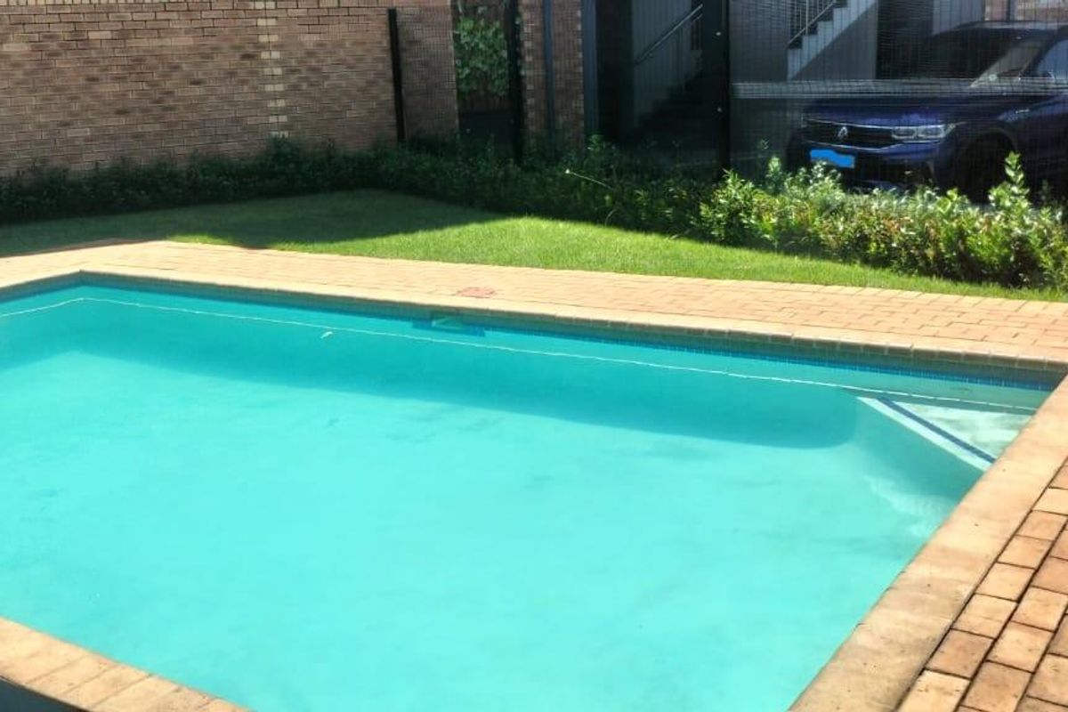 A well-maintained swimming pool area featuring brick paving, a manicured lawn, and secure perimeter fencing.