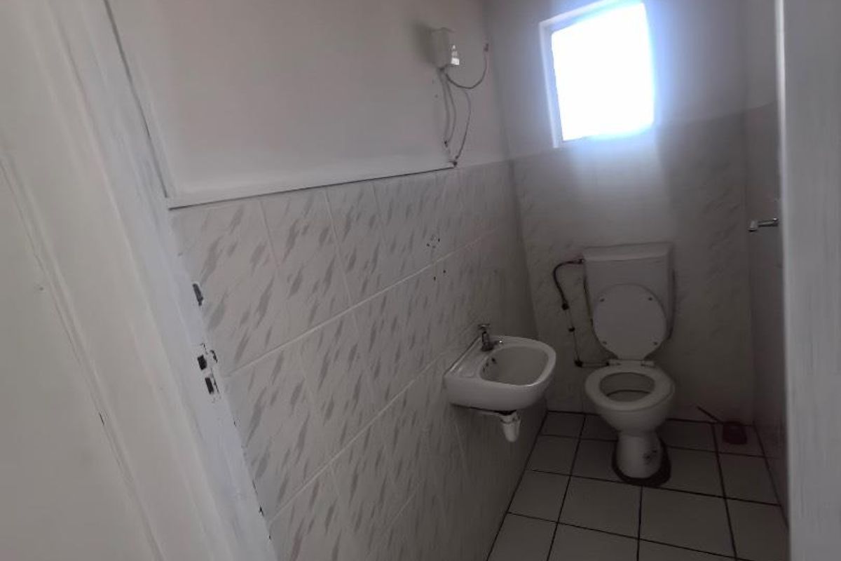 A small, functional guest bathroom featuring a wall-mounted basin, toilet, and tiled walls with a small window for natural light.