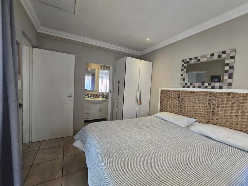 A well-maintained bedroom featuring tiled flooring, built-in cupboards, coved ceilings, and direct access to an en-suite bathroom.