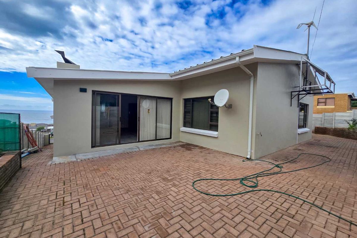 Rear view of the property featuring a paved patio area, sliding glass doors, and exterior wall finishes with a view of the coastline.