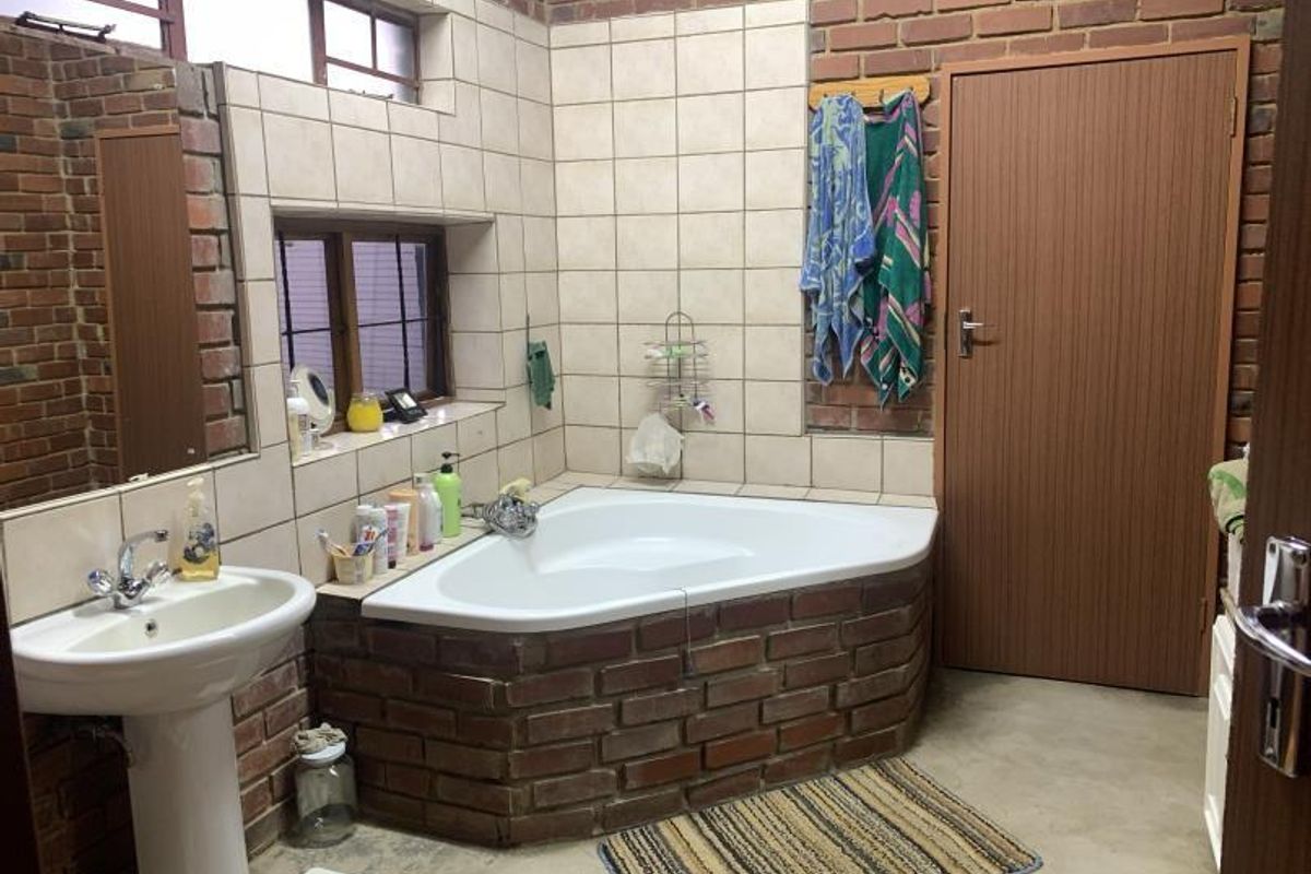 A rustic bathroom featuring exposed brick walls, a corner bathtub with brick surround, and a pedestal basin.