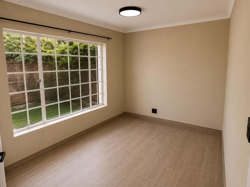 A bright, empty bedroom featuring neutral walls, modern wood-look tiled flooring, and a large grid-pattern window overlooking the garden.